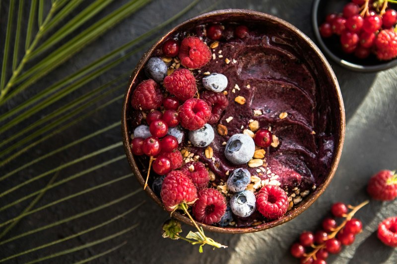 Frozen acai smoothie in coconut shell with raspberries, banana, blueberries