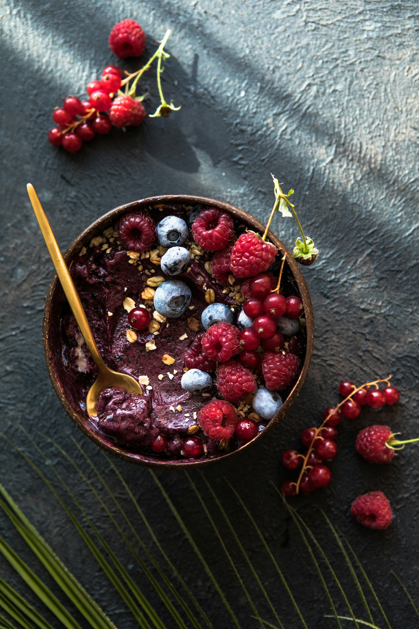 Frozen acai smoothie in coconut shell with raspberries, banana, blueberries