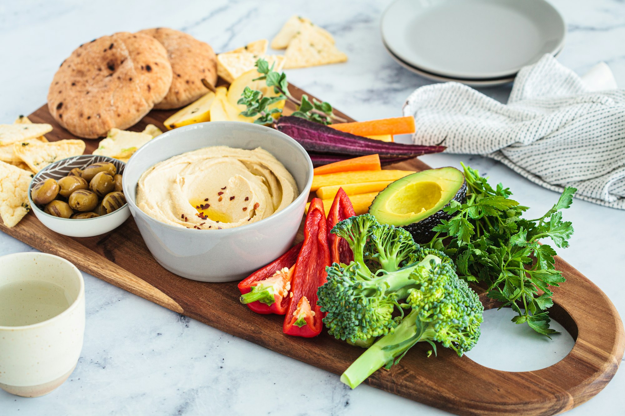 Vegetarian snack board with hummus, vegetables, fruits, olives, pita and crackers.