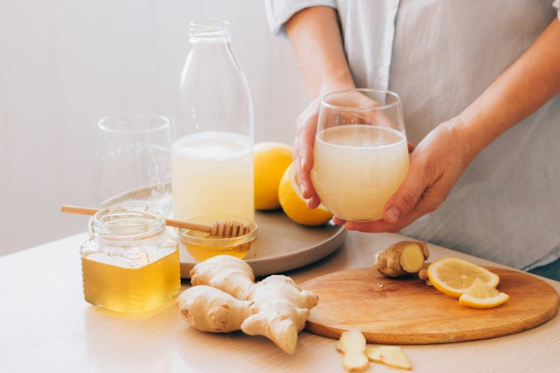 Women's hands hold glass with drink made from ginger root honey lemon, freshly prepared antioxidant